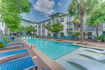 A pool surrounded by blue lounge chairs and palm trees.